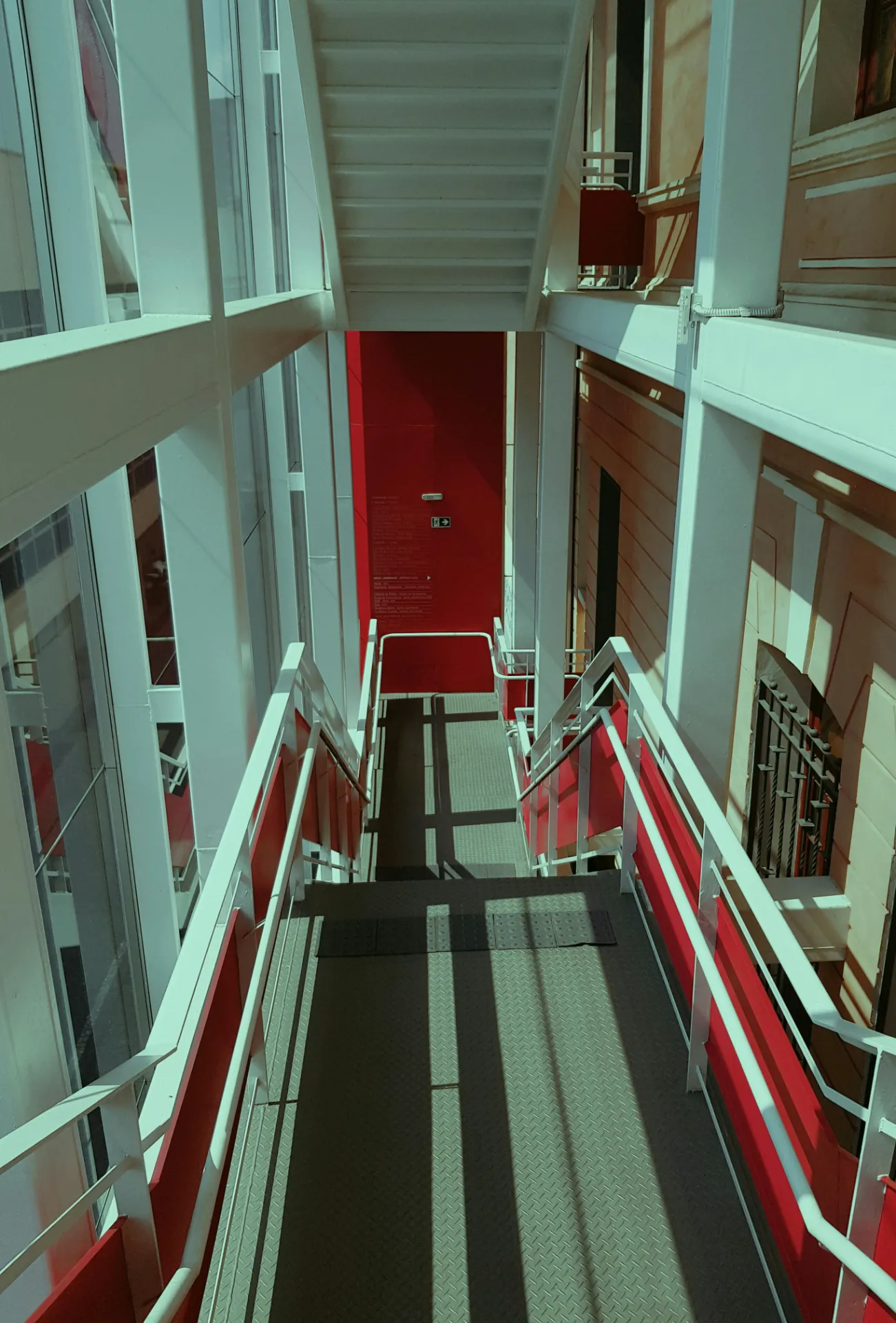 Escalier métallique moderne blanc et rouge avec verrière lumineuse.